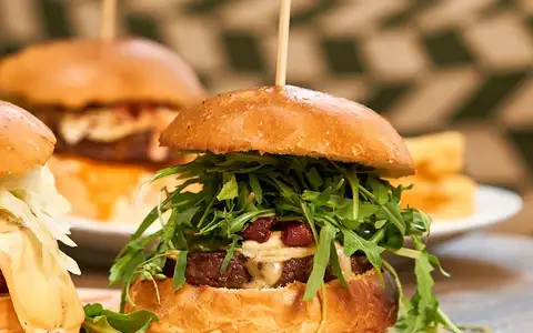 Gros plan sur un burger garni de roquette, servi sur une planche en bois