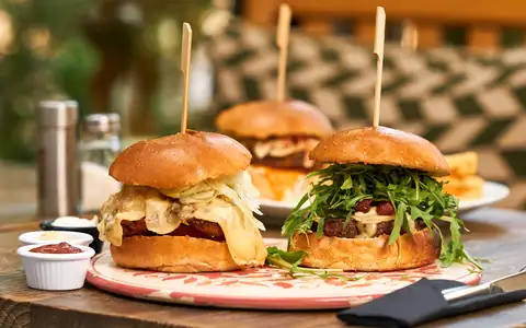 Burgers garnis de roquette et de chips servis sur une planche en bois en terrasse