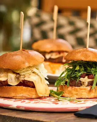 Burgers garnis de roquette et de chips servis sur une planche en bois en terrasse