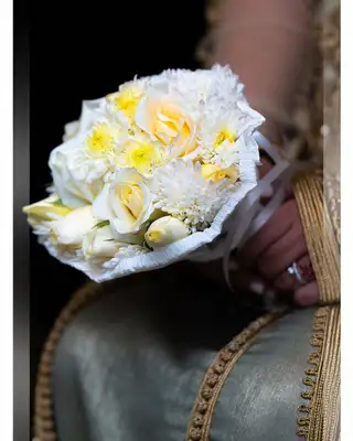 Bouquet de roses blanches et jaunes posé sur le caftan de la mariée