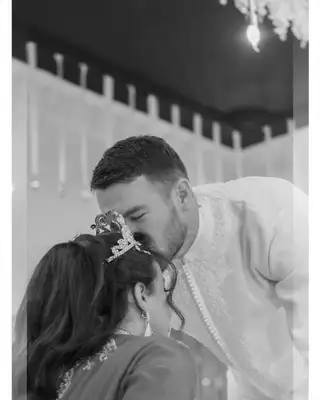Le marié embrasse le front de la mariée pendant la soirée, en noir et blanc