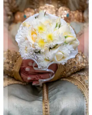 Mains de la mariée en caftan doré tenant un bouquet de roses blanches