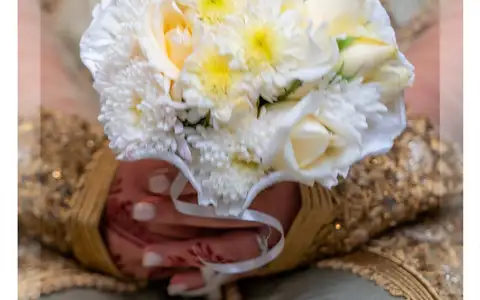 Mains de la mariée en caftan doré tenant un bouquet de roses blanches
