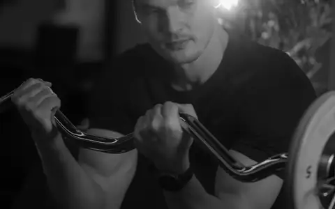 Athlète travaillant les biceps à la barre EZ en salle de sport, en noir et blanc