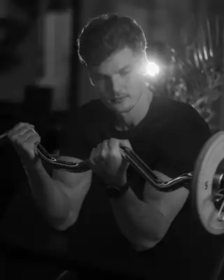 Athlète travaillant les biceps à la barre EZ en salle de sport, en noir et blanc