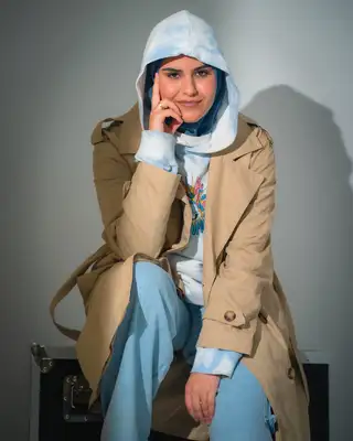 Modèle en trench et capuche bleu ciel, la main sur la joue