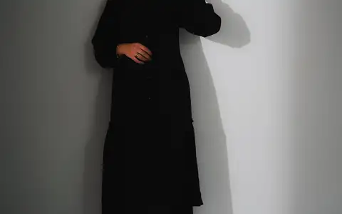 Silhouette en robe noire longue sur fond blanc, en plan pied