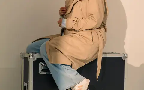 Modèle en trench beige et foulard bleu assise sur une flight case en studio