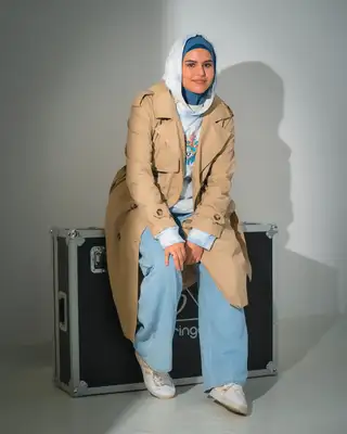 Modèle en trench beige assise face à l'objectif sur fond gris
