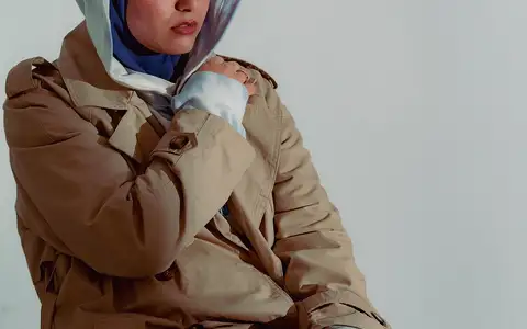 Modèle en trench camel et capuche bleue, ombre portée sur le fond blanc