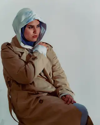 Modèle en trench camel et capuche bleue, ombre portée sur le fond blanc