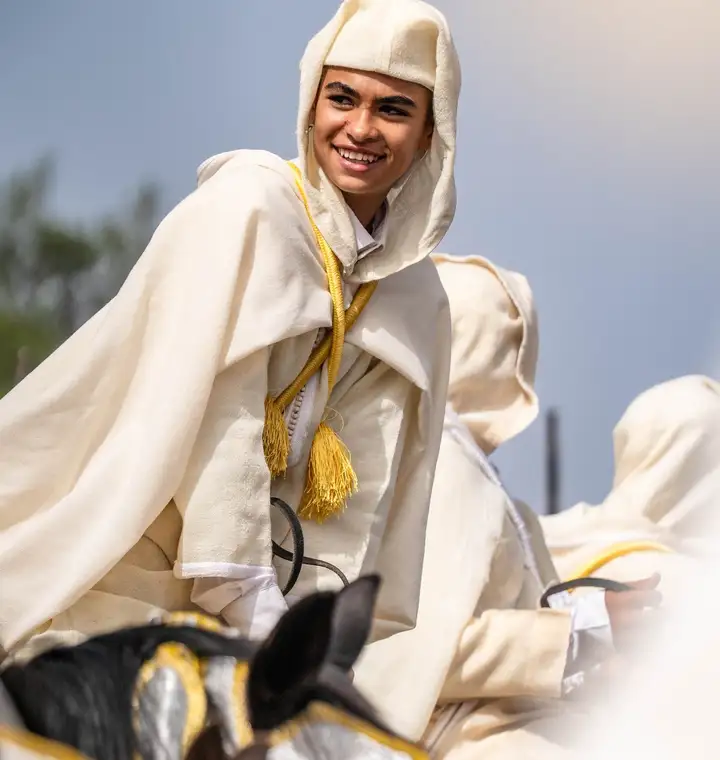 Cavalier souriant en tenue blanche traditionnelle sur son cheval lors d'un moussem